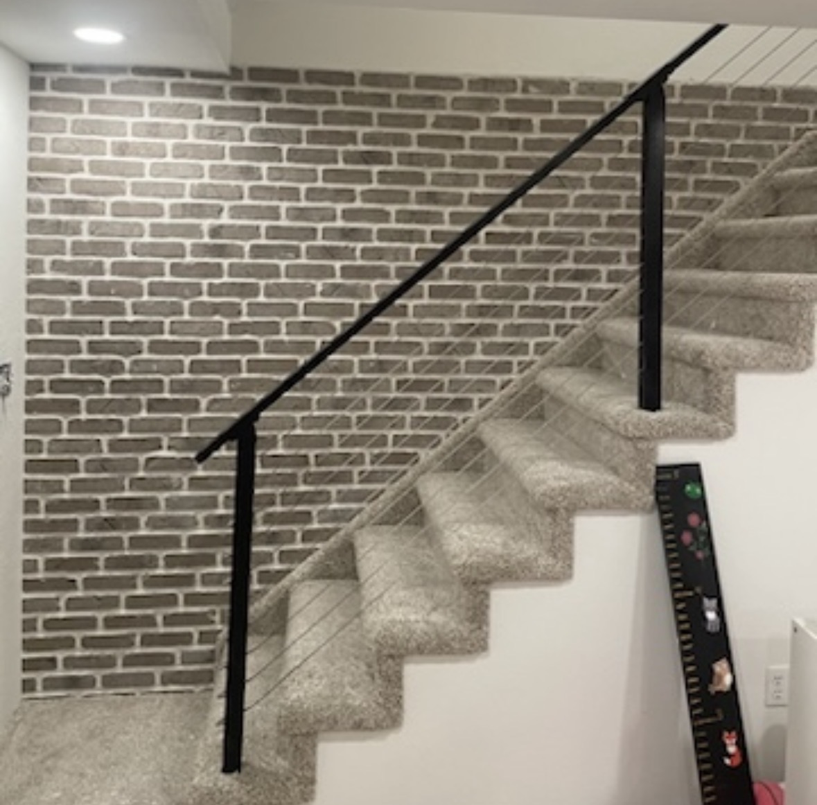 Finished basement stair — Faux-brick accent wall, carpeted run, welded steel railing